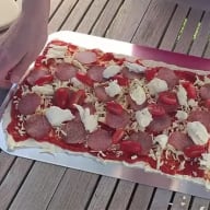 En utkavlad pizzadeg på en plåt toppad med tomatsås, skinka och bitar av mozzarella.