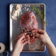 En person förbereder kött på en bricka med kryddor och snöre bredvid.