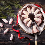 En tallrik med chokladgodis i form av en krans omgiven av granris, band och ljusslingor på ett träbord.