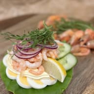 Närbild av en räkmacka toppad med räkor, skivat ägg, lök, dill och en citronskiva.