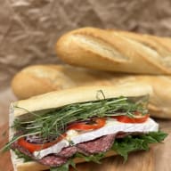 Baguettesmörgås fylld med salami, brieost, salladsblad, skivad lök, paprika och groddar.