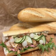 Baguettesmörgås fylld med friterad kyckling, skivad gurka, inlagda pärllökar och sallad.