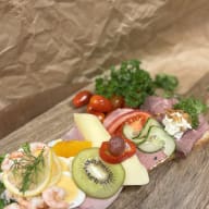 Öppet smörgåsbricka med flera pålägg, inklusive räkor, ägg, ost, kiwi och skivat kött.