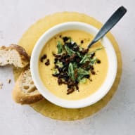 Slät pumpasoppa ligger i en skål med chorizosmul som topping och bröd vid sidan av.
