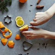 Händer som skär en skalad apelsin som ligger på ett grått bord