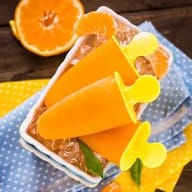 Glasspinnar med fruktsmak ligger i en skål bredvid en halv citrusfrukt på en duk.