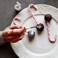 En person målar på chokladbollar med en pensel på en tallrik bredvid polkagrisar.