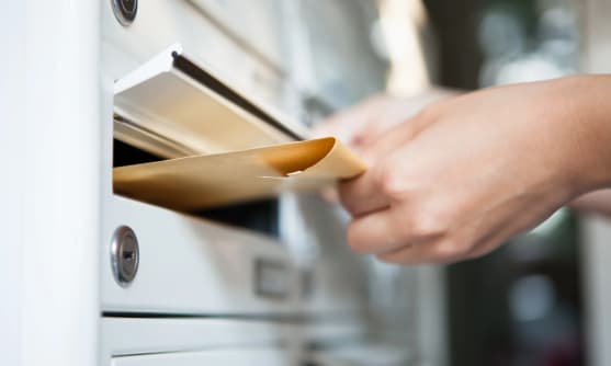 En hand som postar ett kuvert i en brevlåda.