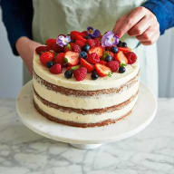 Tårtan garneras med färska bär, ätbara blommor och mynta.