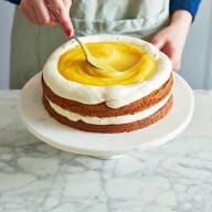 Lemon curd fördelas i mitten av tårtan med hjälp av en sked