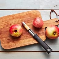 Röda äpplen och en äppelurkärnare på en skärbräda. Ett av äpplena är urkärnat och har ett hål i mitten.