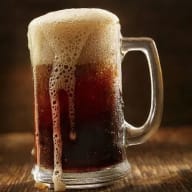 Ett ölglas fyllt med mörk dryck och skummande överdel står på en träyta.