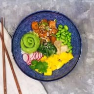 En tallrik med olika maträtter innehållande grönsaker, sallad och kött serveras bredvid ätpinnar på en bordsyta.