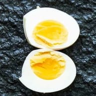 Hårdkokt ägg med lätt grynig gula, delat i halvor mot svart botten.