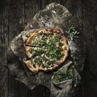 En pizza som ligger på mörk bakgrund. Pizzan är toppad med grönt.