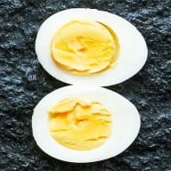 Kokt ägg med grynig, hårdkokt gula som släpper från vitan, delat i halvor mot svart botten.