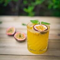 En dryck i ett glas med passionsfrukt och mynta står på ett träbord bredvid halvor av passionsfrukt.
