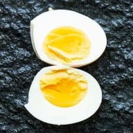 Hårdkokt ägg med hård gula, delat i halvor mot mörk botten.