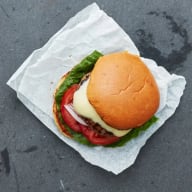 En hamburgare med sallad och tomat ligger på ett vitt papper.