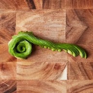 En avokado skuren i en lång spiral ligger på en skärbräda.