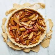 En paj fylld med skivade frukter ligger på ett bakplåtspapper.