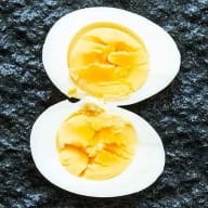 Kokt ägg med grynig gula som börjat släppa från vitan, delad i halvor mot svart botten.