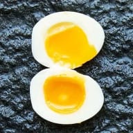 Löskokt ägg med rinnande gula, delat i två mot mörk botten.