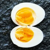 Kokt ägg med nästan helt hårdkokt gula, delad i halvor mot svart bakgrund.