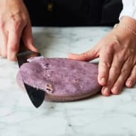 En person skär i en rund, platt matvara på en marmoryta med en kniv.