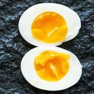 Kokt ägg med lite rinnande gula i mitten av ägget, delat i halvor mot svart bakgrund.