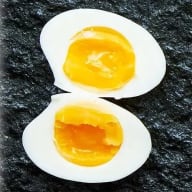 Mjukkokt ägg med halvlös gula, delat i halvor mot mörk botten.