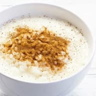 En skål med vit gröt eller yoghurt toppad med ett brunt pulver.