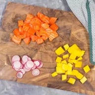 En skärbräda med bitar av lax, rädisa och mango.