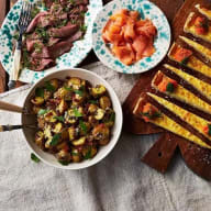 En tallrik med kött, en tallrik med lax, en skål med grönsaker och brödskivor på en träskärbräda.