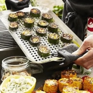 En person förbereder sushirullar på ett galler över en grill, med en burk och färdiga sushirullar synliga i förgrunden.
