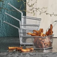 En metallkorg med pommes frites står bredvid två tomma korgar på ett bord mot en vägg med växter.