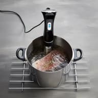 En elektrisk apparat står i en kastrull med kött på ett metallgaller.