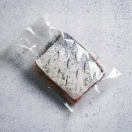 En bit ost insvept i plastfolie ligger på en yta.
