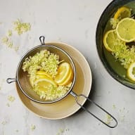 En sil med citronskivor och fläderblommor står på en tallrik bredvid en skål med liknande innehåll.