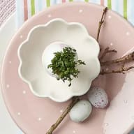 En tallrik med en blomformad skål innehållande små gröna växter, två små ägg och en kvist.