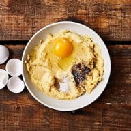 En skål med hummus toppad med en äggula och kryddor står på ett träbord bredvid äggskal.