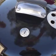 En grill med ett handtag och en termometer på locket.