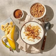 En frukostbricka med yoghurt, granola, banan och kanel.