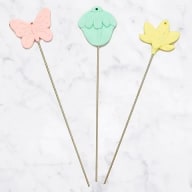 Tre dekorativa figurer på pinnar: en fjäril, en muffin och ett löv.