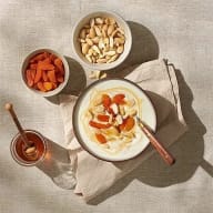 En skål med yoghurt och toppingar står på en duk tillsammans med två mindre skålar och en honungsburk.
