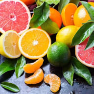 Citrusfrukter och gröna blad ligger på en mörk yta.