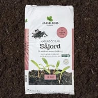 En förpackning med såjord från Hasselfors Garden står på mörk jord.