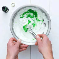 Bunke med marängsmet som färgats grön med hjälp av karamellfärg och en hand som vispar