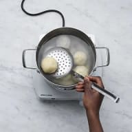 En person håller en slev över en kastrull med dumplings på en elektrisk kokplatta.