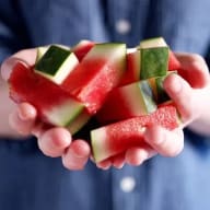 En person håller bitar av vattenmelon och gurka i sina händer.